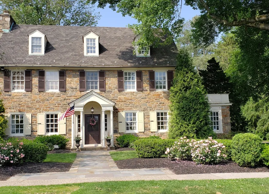 A stone-front American colonial home with an American flag on the porch.