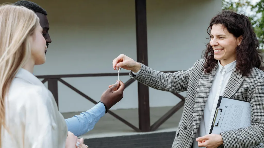 A real estate professional handing keys to a couple in front of a home. Franks Financial LLC works with sellers and agents of every background.