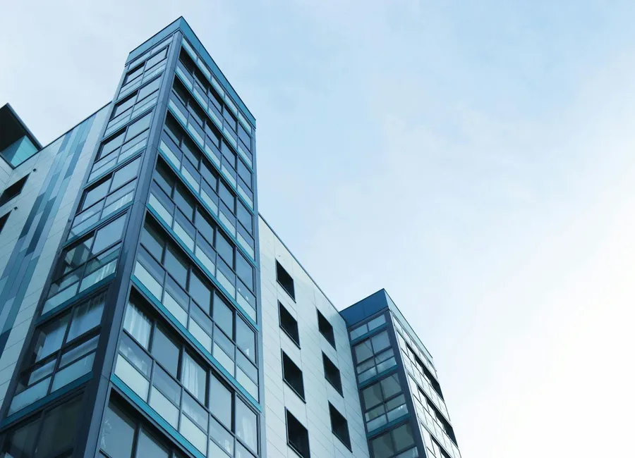 A modern glass-and-steel multi-family apartment building seen from the street.